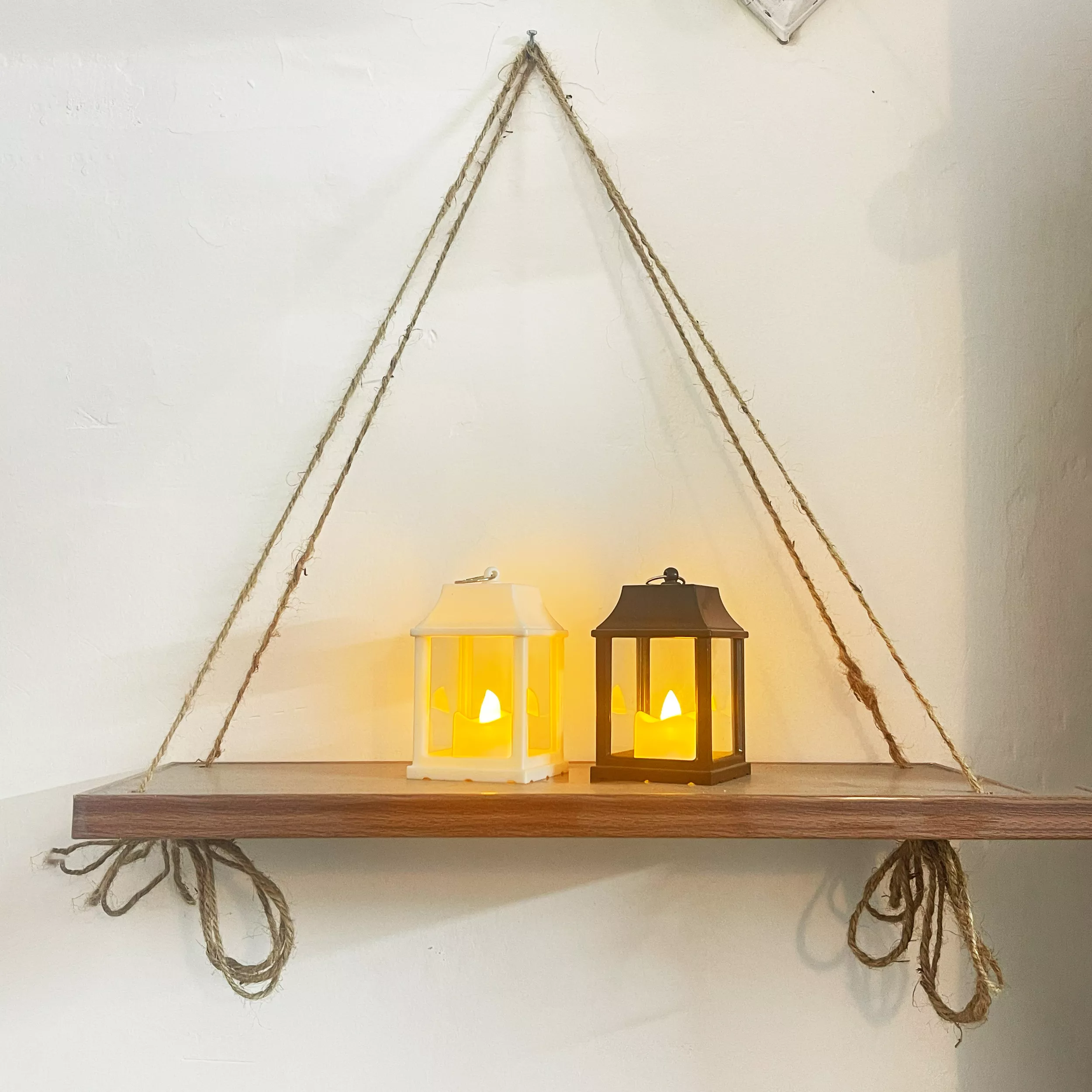 Hanging wooden shelf with two lit lanterns on a white wall.