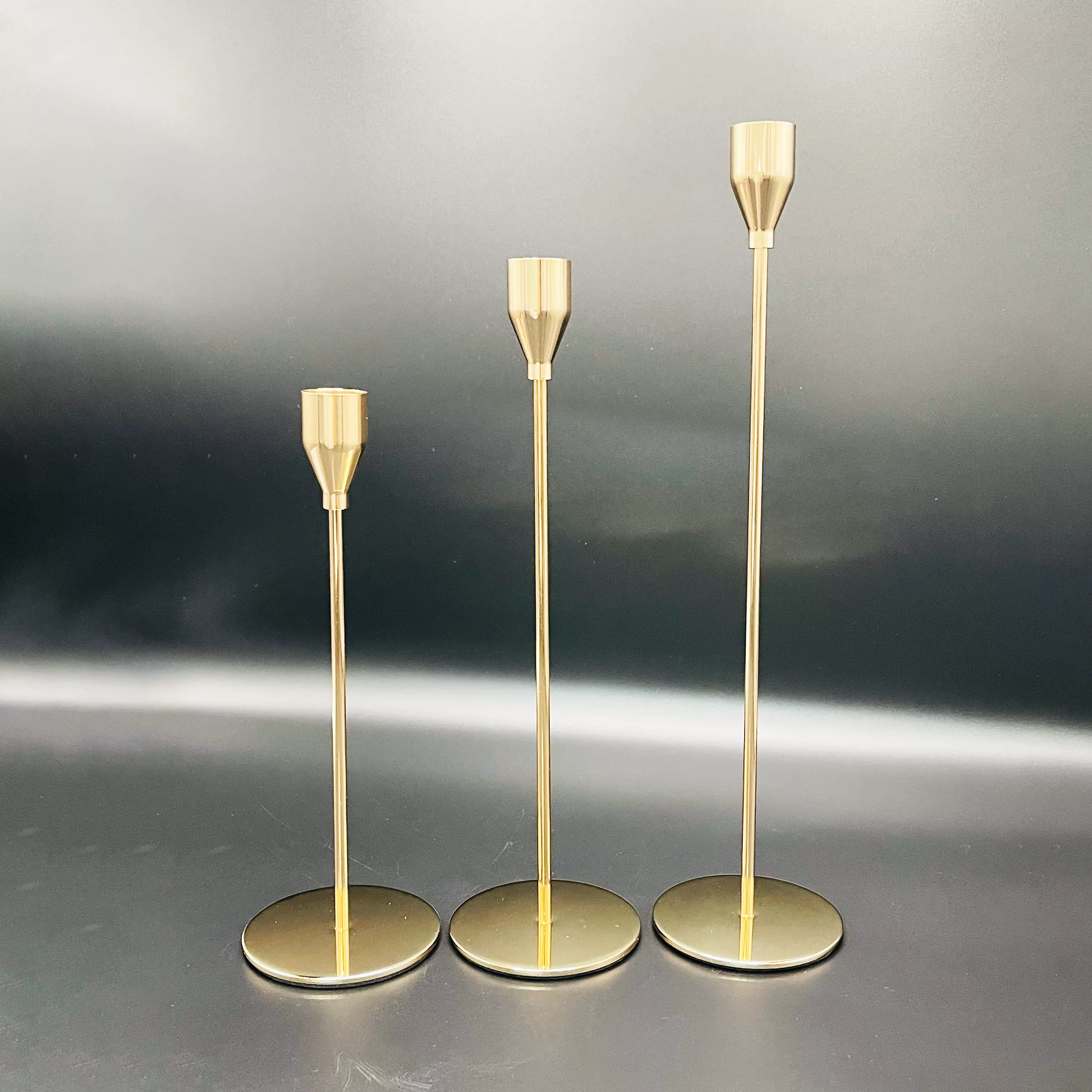 Three polished rose Golden Metal Candle Stand with cylindrical tops transitioning into conical shapes.