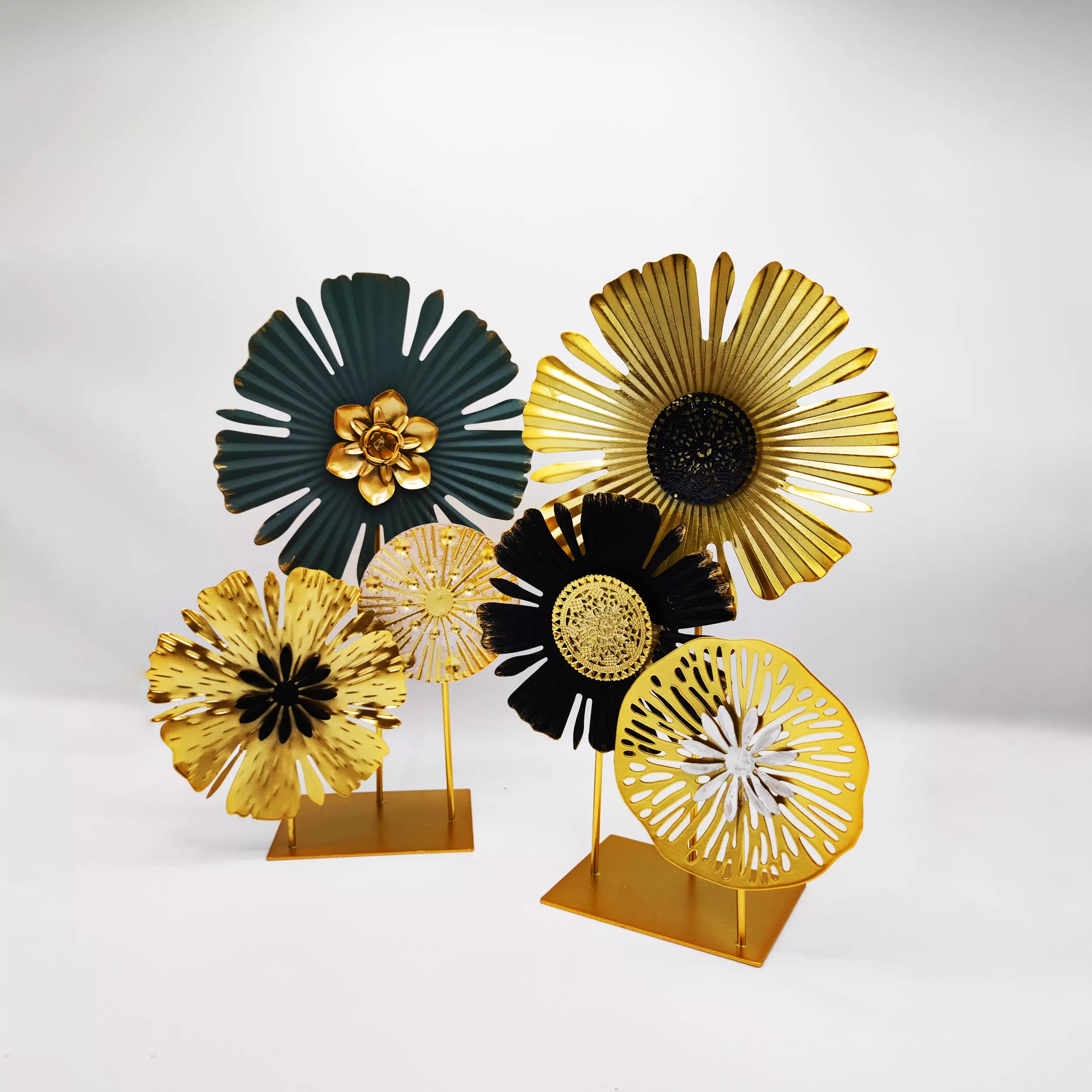 Two sets of modern metallic flower tabletop decor, in gold, black, and dark green, on gold stands, against a light background.