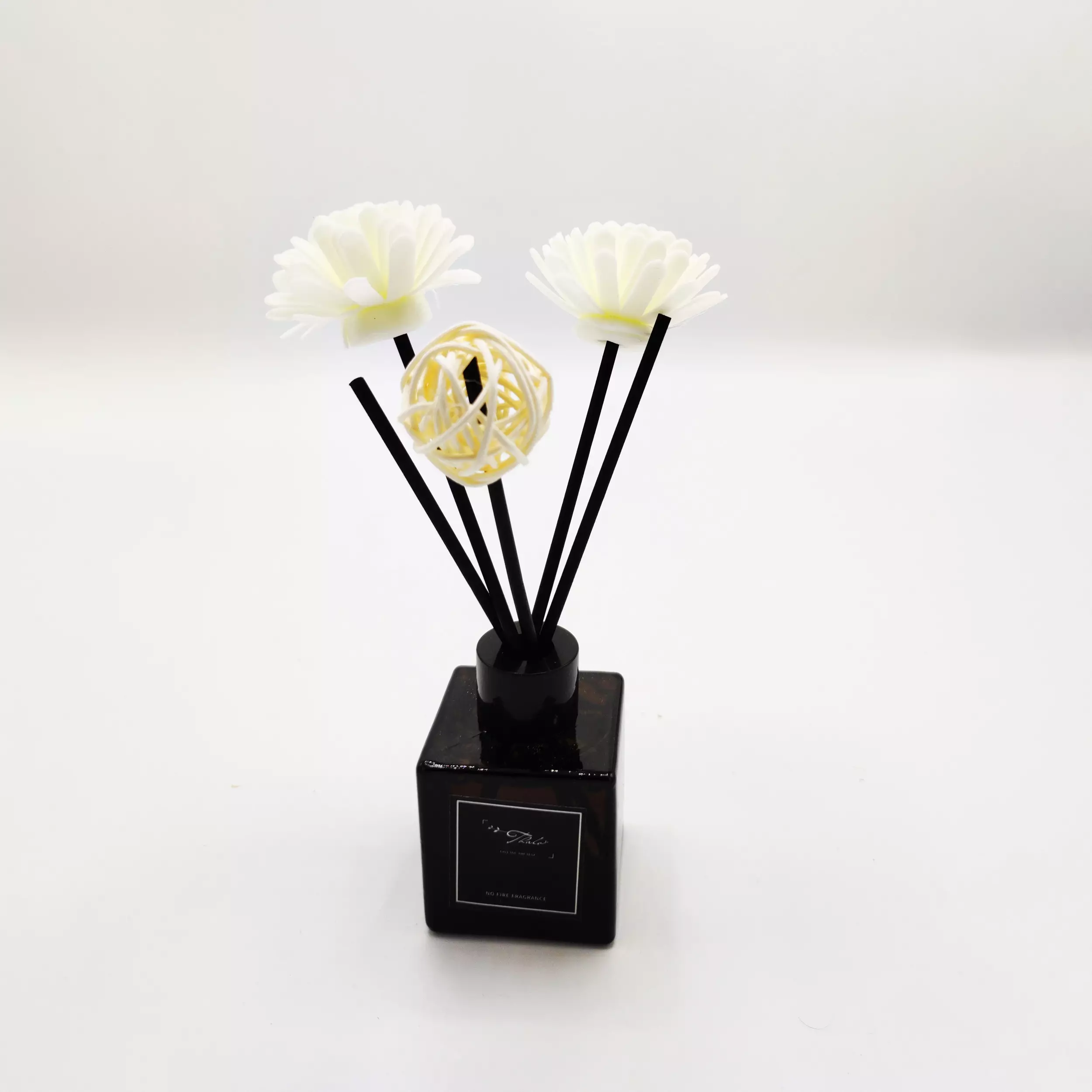 A black square Fragrance diffuser with white flower bottle and a yellow decorative ball.